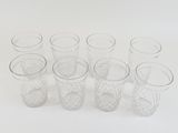 six clear glass shot glasses lined up on a white surface