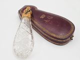 une bouteille en verre et un étui en cuir posés sur une surface blanche