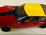 une petite voiture rouge avec un toit jaune posée sur une surface blanche