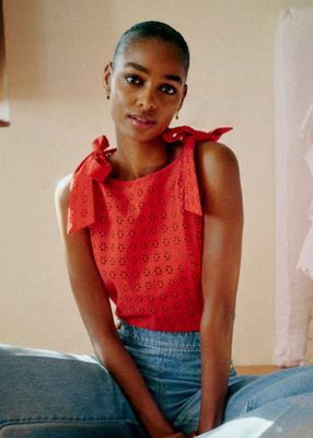 a woman sitting on a bed wearing a red top