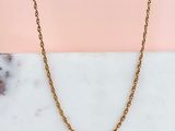 un collier à chaîne en or posé sur une surface en marbre, sur fond rose