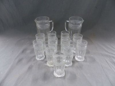 six pichets en verre transparent et un pichet posé sur une nappe blanche