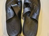une paire de sandales noires posées sur une surface blanche, avec une bouteille d'eau
