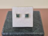 une paire de boucles d'oreilles en émeraude posée sur un bloc de marbre