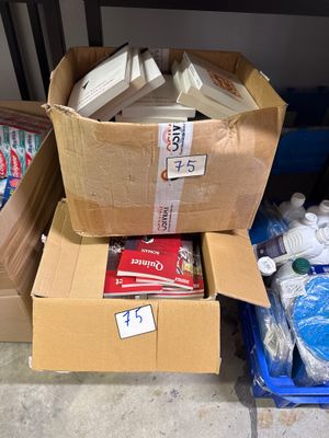 Plusieurs cartons de fournitures sont empilés les uns sur les autres par terre.