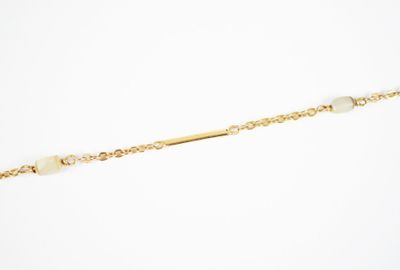 a close up of a gold chain with a white bead on it