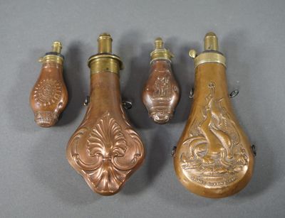 Quatre flacons de parfum en laiton vieilli sont alignés sur une surface grise