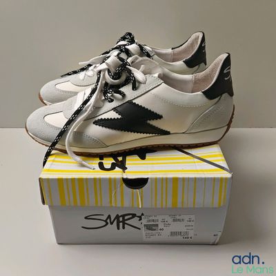 une paire de baskets blanches et noires posée sur une boîte