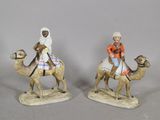 deux figurines représentant des personnes à dos de chameau, posées sur un fond gris