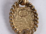 a gold pendant with a rope around it on a white surface
