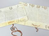 un vieux document auquel est attachée une chaîne, à côté d'un collier