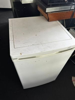 un petit réfrigérateur blanc posé dans une pièce, à côté d'un bureau