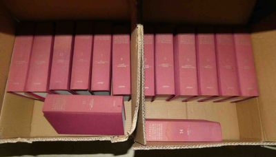 Plusieurs livres roses se trouvent dans une boîte en carton posée sur une table