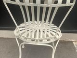 a white metal chair that is sitting on the sidewalk