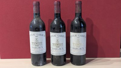 three bottles of red wine sit on a table in front of a red wall