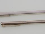 two silver colored pens sitting next to each other on a white surface