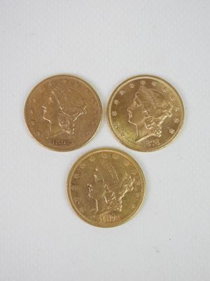 trois pièces d'or posées l'une à côté de l'autre sur une surface blanche