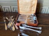 Plusieurs couverts sont posés sur une table en bois, à côté d'un coffret rempli de fourchettes, de cuillères et de cuillères