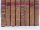 six old books are lined up in a row on a white surface