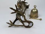 brass figurines of a dragon and a bell on a white surface