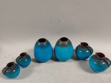 six blue glass vases are arranged in a circle on a white surface