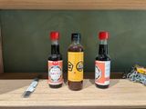 three bottles of sauce on a shelf next to a knife