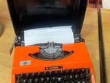 une machine à écrire orange posée sur une table, avec un clavier noir