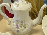 a white tea pot with purple flowers on it on a table