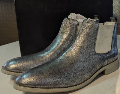 des bottines en cuir argenté posées sur une table blanche, avec une boîte noire en arrière-plan