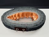 une sculpture en béton et en cuivre posée sur une surface blanche