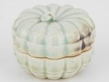 une boîte en forme de citrouille, blanche et verte, posée sur une surface blanche