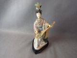 figurine représentant une femme jouant d'un instrument de musique, posée sur un socle noir