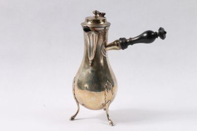 une cafetière ancienne en métal argenté, avec une poignée noire sur fond blanc