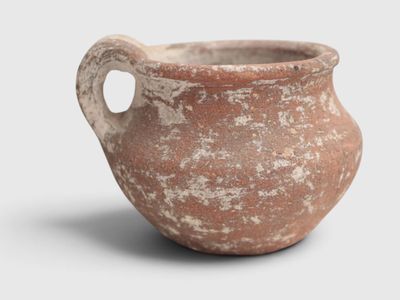 a clay pot with a handle on a white surface