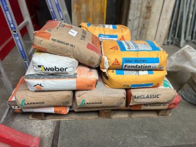 plusieurs sacs de ciment posés sur une palette devant un bâtiment
