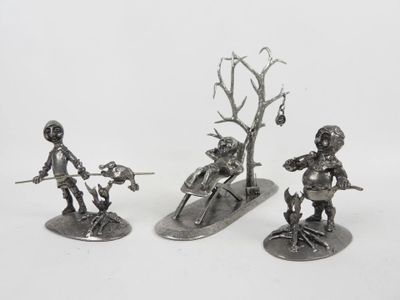 three silver metal figurines of a man and a woman on a snowboard