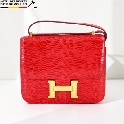 un sac à main rouge orné d'un « H » doré, posé sur une surface blanche