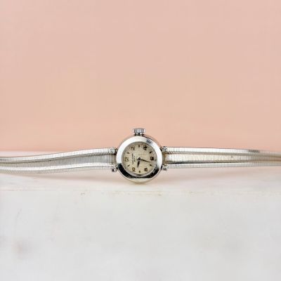 une montre en argent montée sur un bracelet en argent, sur fond rose