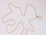 un collier en or orné d'une feuille, posé sur une surface blanche
