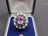 une photo d'une bague dans un écrin, avec des perles et une pierre rose