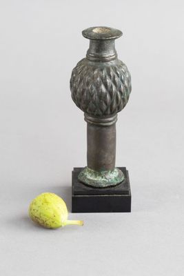 un petit vase en métal contenant une poire, posé sur un socle