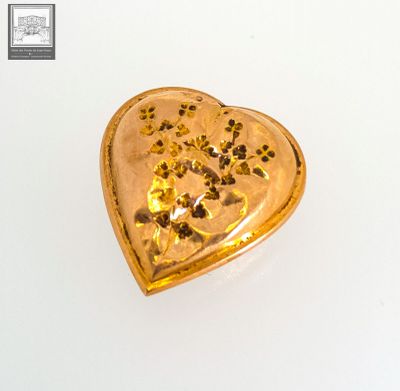 a gold heart shaped brooch on a white surface