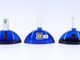 three blue glass bottles with a clock on top of them on a white surface