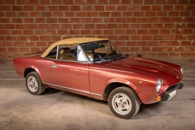 a red car with a tan top parked in front of a brick wall