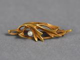 a close up of a gold brooch with a pearl in it