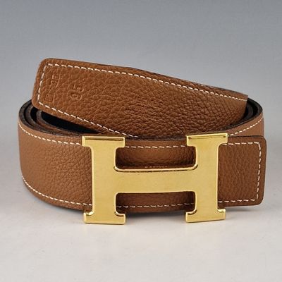 ceinture en cuir marron avec une boucle en forme de H dorée sur fond blanc