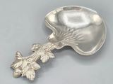 an antique silver spoon with leaves on it on a gray surface