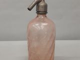 une vieille bouteille en verre rose munie d'un bec verseur en métal, posée sur une table