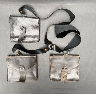 deux porte-monnaie en cuir argenté avec une lanière noire, posés sur un fond gris