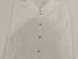 La chemise est blanche et comporte des boutons au niveau du col.